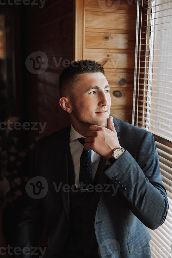 A stylish portrait of the groom preparing for the wedding ceremony in the morning. Groom's morning. Preparation for the groom's morning. The groom puts on a jacket. The confident look of a mature man. photo