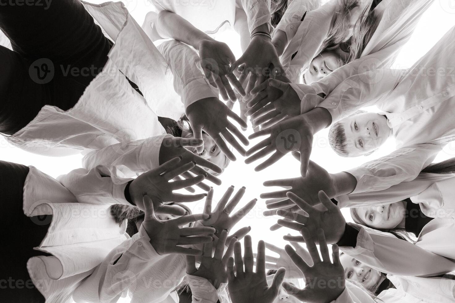 A large group of smiling young people standing, hugging, looking at the camera and stretching their arms down. Group of cheerful teenage people in a circle looking down. Low viewing angle. Copy space. photo