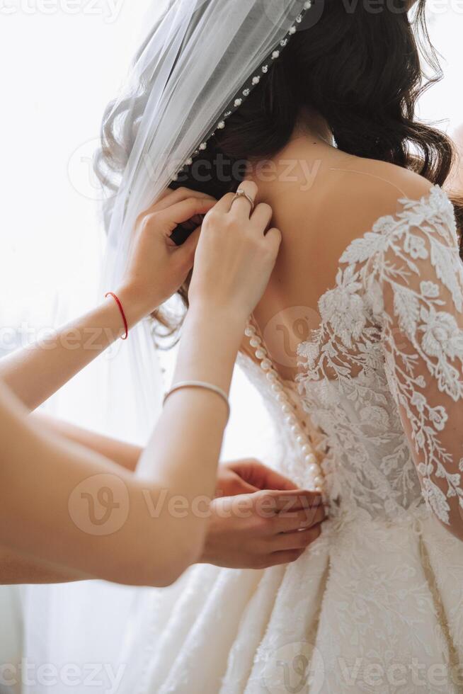 Mañana de el novia. el de la novia mucama de honor ayuda el novia cordón arriba su vestido, sujetar botones en el vestir o mangas novias ayuda el novia sujetar su vestir foto