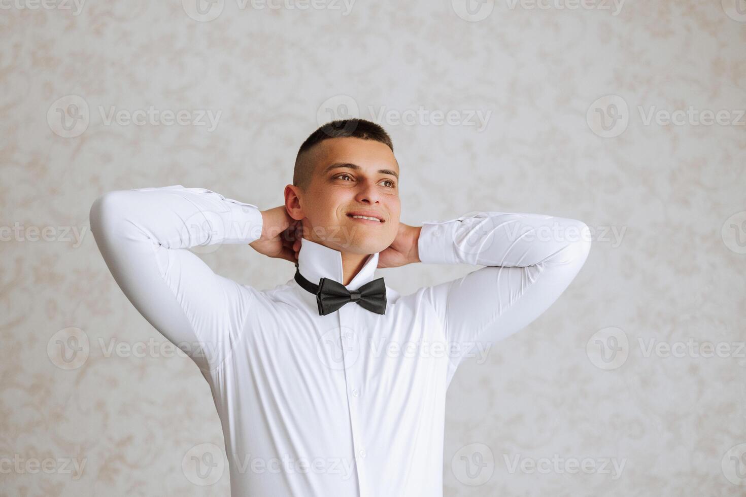 A stylish groom is tying his tie, preparing for the wedding ceremony. Groom's morning. A businessman wears a tie. The groom is getting ready in the morning before the wedding ceremony. photo