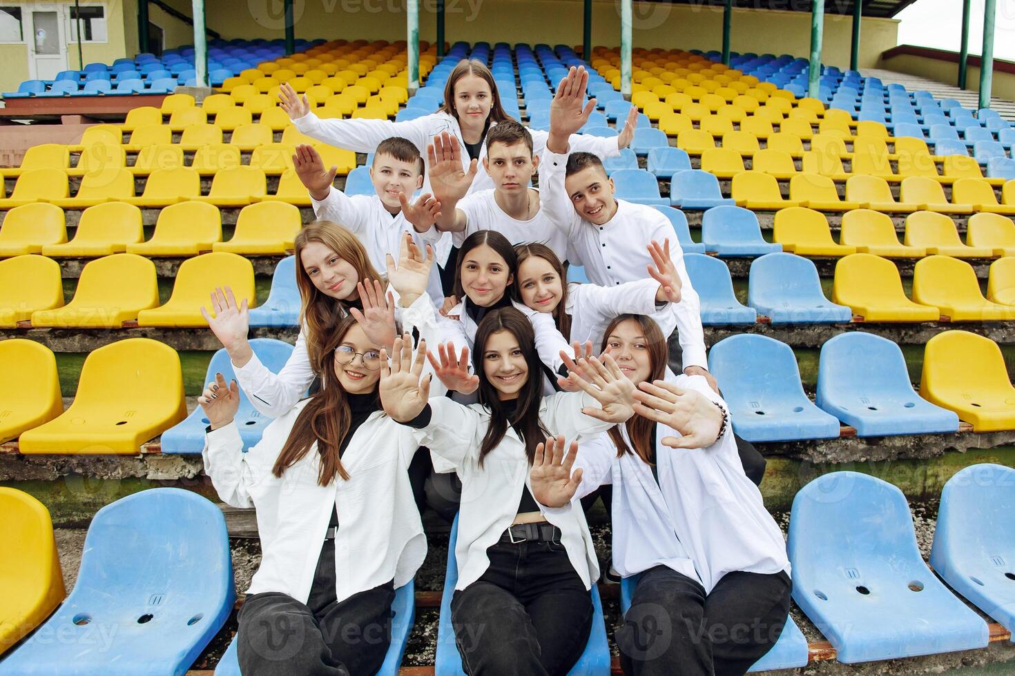 A group of many happy teenagers dressed in the same outfit having fun and posing in a stadium near a college. Concept of friendship, moments of happiness. School friendship photo