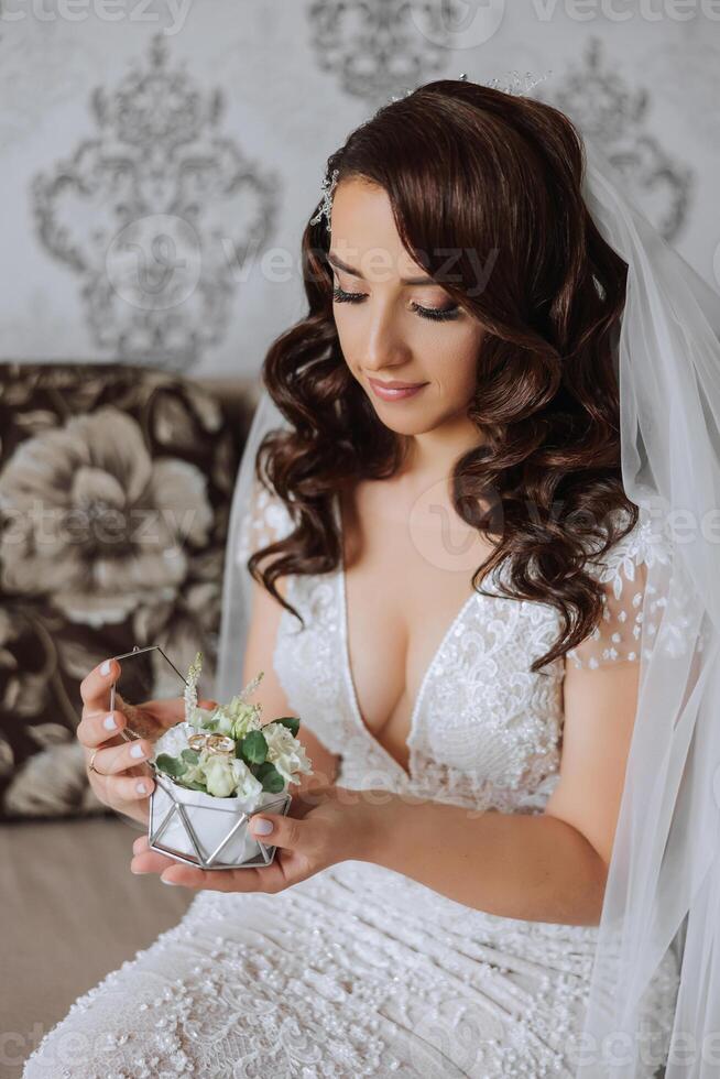 A wonderful beautiful portrait of a young bride. Beautiful bride with wedding makeup and jewelry wreath on long curly hair. Wedding photo model with brown eyes in a beautiful interior.