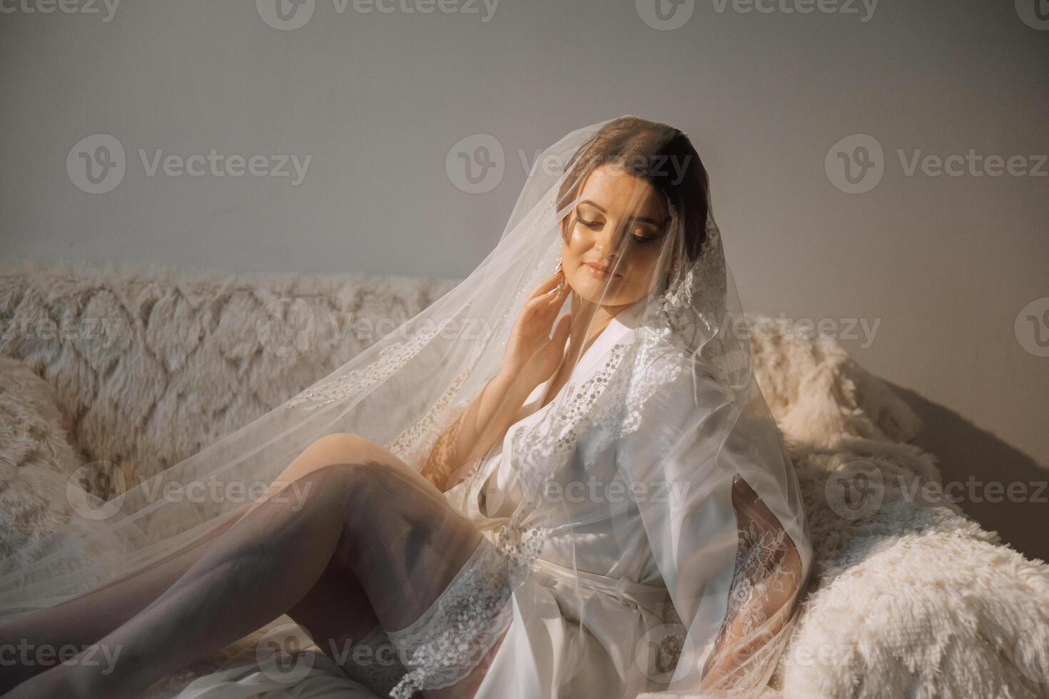 Nice cute girl in a boudoir robe. Happy beautiful bride under veil. Fashion, beauty, style. Morning of the bride. Beautiful bride with stylish make up and hair style. photo