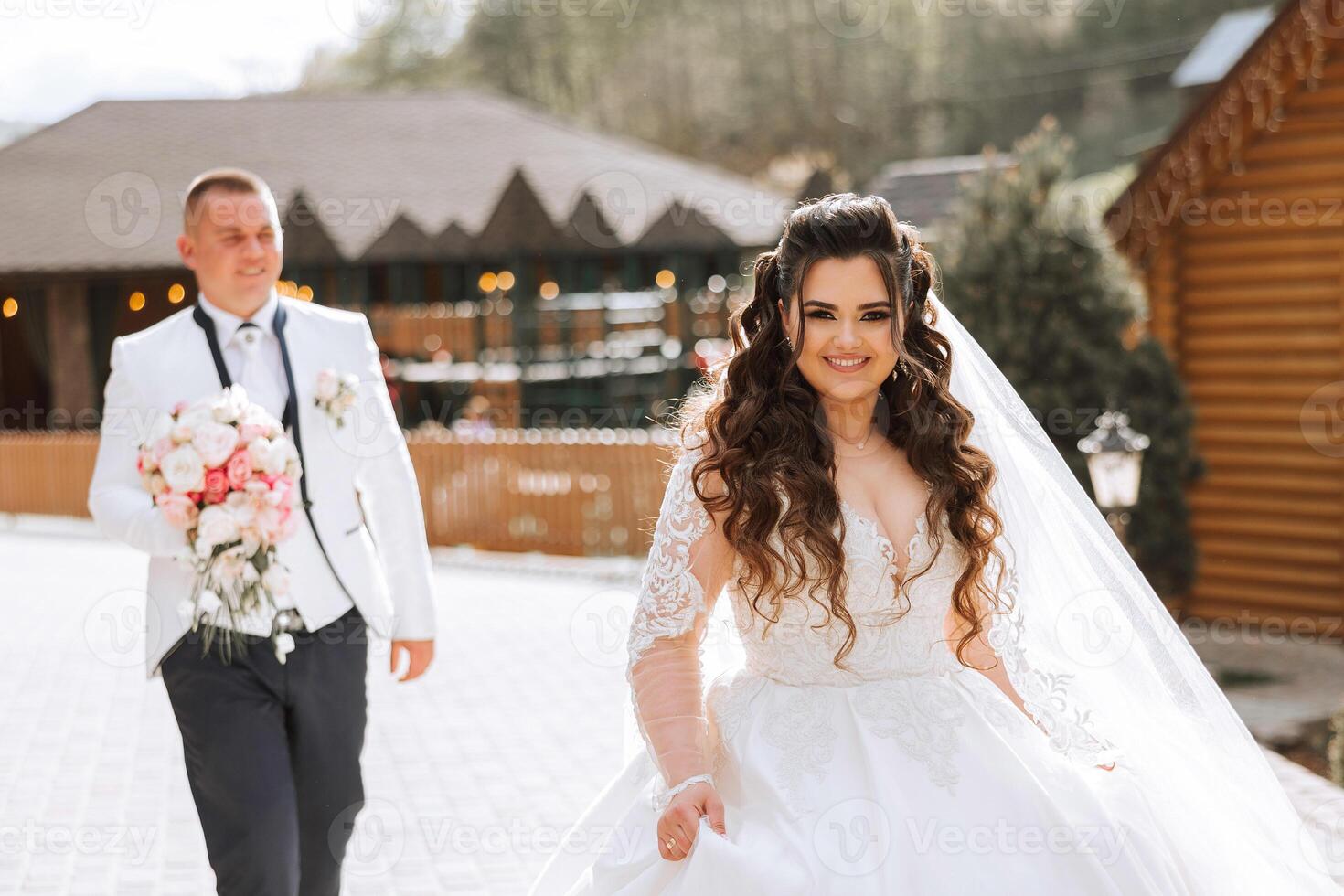 A beautiful young bride, in a summer park, walks ahead of her groom. Beautiful wedding white dress. Walks in the park. A happy and loving couple. photo