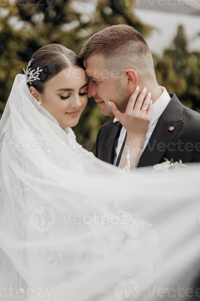 The bride in an elegant dress with a bouquet and the groom in a classic suit are walking in the garden, holding hands. photo
