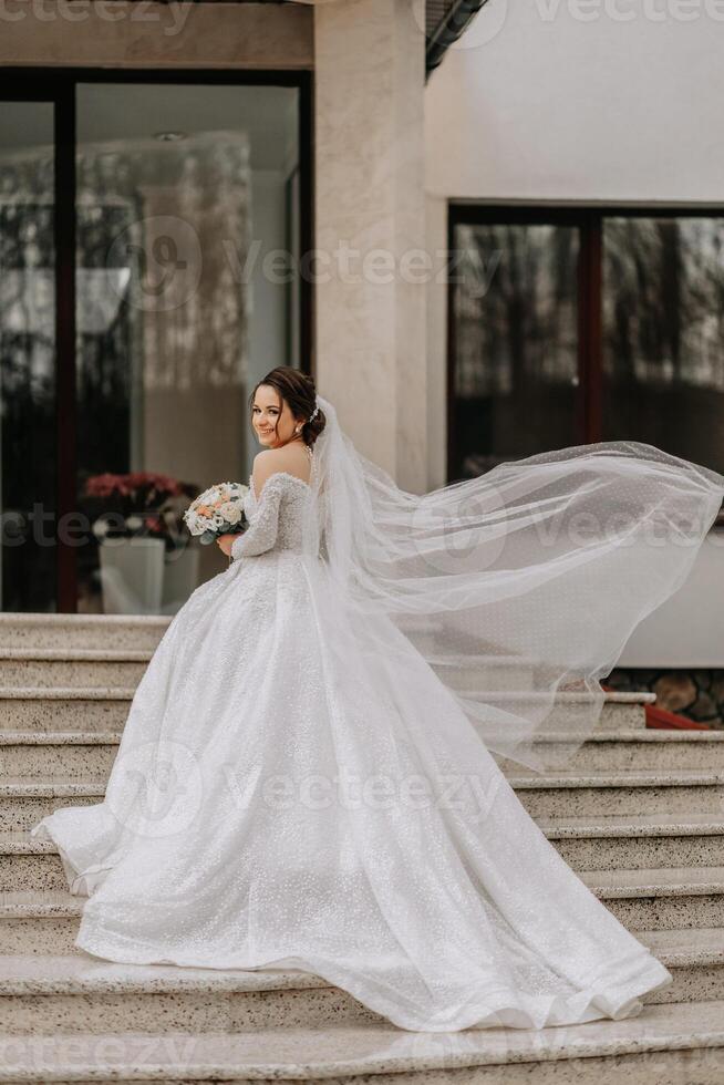 The bride in a white dress with a train and a long veil poses in nature, holding a bouquet. Walk. Winter wedding in nature. photo