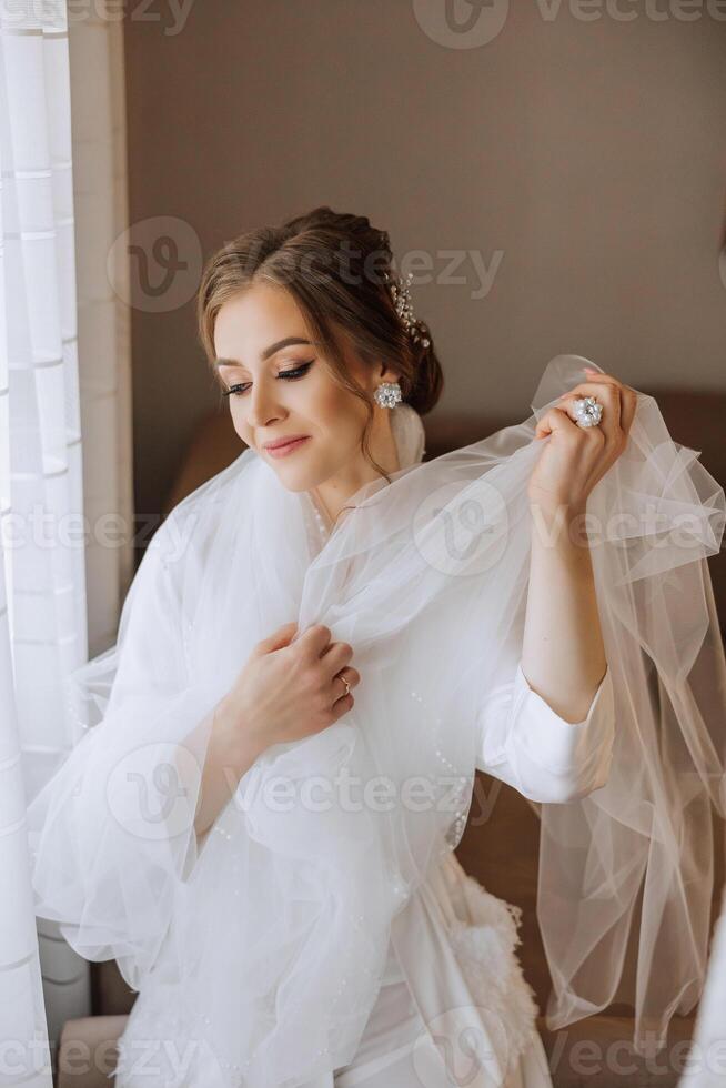 A beautiful brunette bride with a tiara in her hair is getting ready for the wedding in a beautiful robe in boudoir style. Close-up wedding portrait, photo. photo