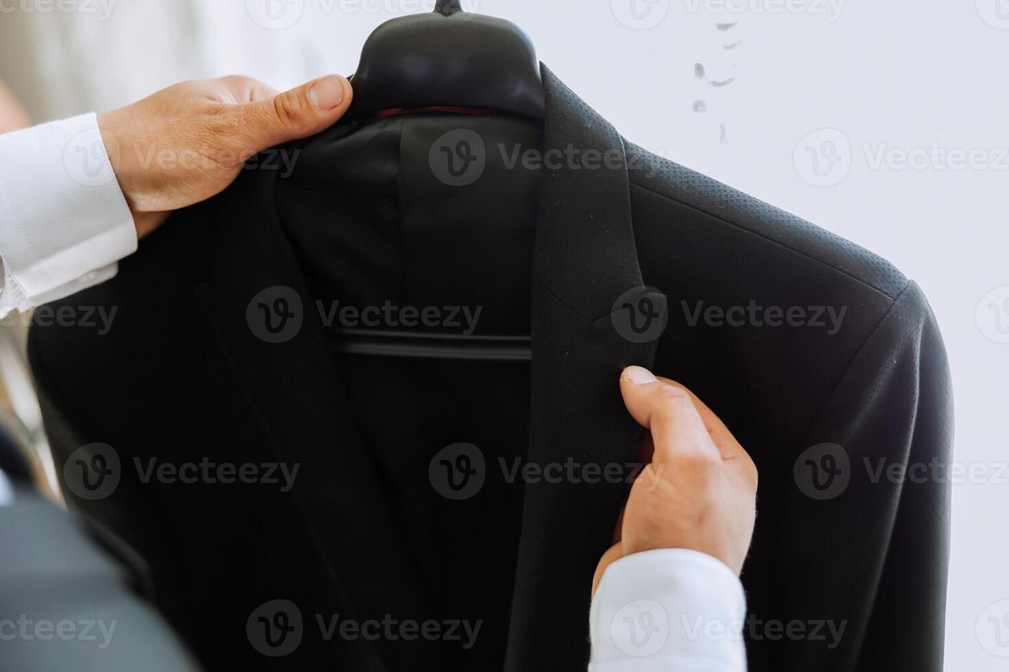 the man holds his black jacket on a hanger in his hands. The groom is preparing for the wedding ceremony. Detailed close-up photo of hands