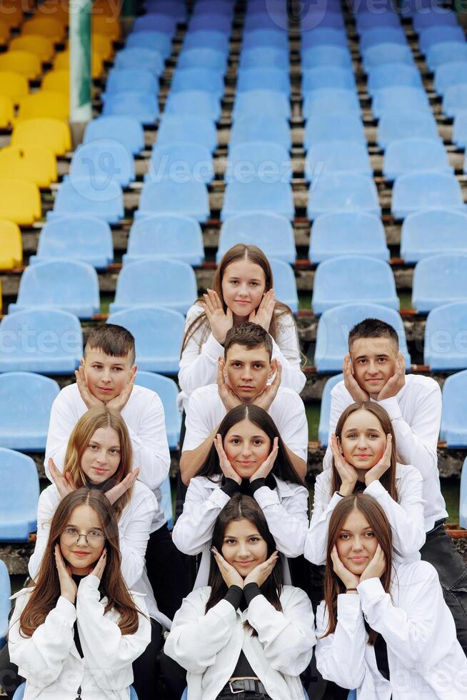 A group of many happy teenagers dressed in the same outfit having fun and posing in a stadium near a college. Concept of friendship, moments of happiness. School friendship photo