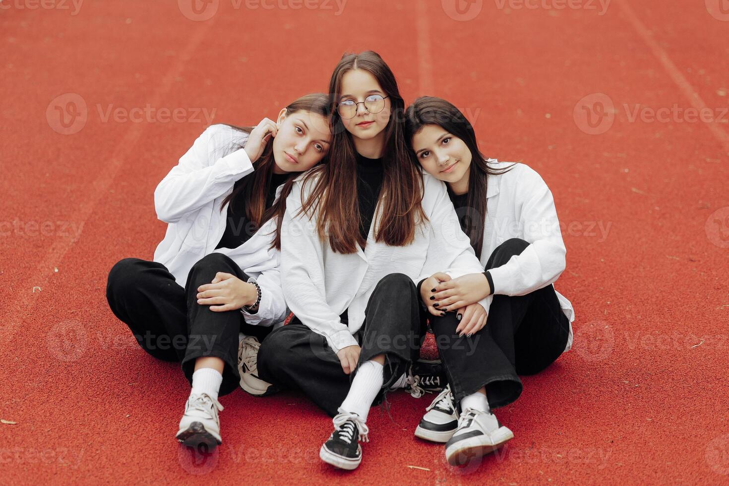 Portrait of three teenage girls in casual clothes sitting in a stadium and posing looking at the camera. Concept of friendship. A moment of happiness. photo