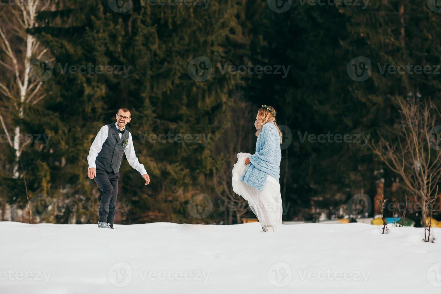 Young couple bride and groom playing in the winter nature on the background of the forest. They run and throw snow. Jump. Have a good time laughing. The concept of a winter wedding in the mountains photo