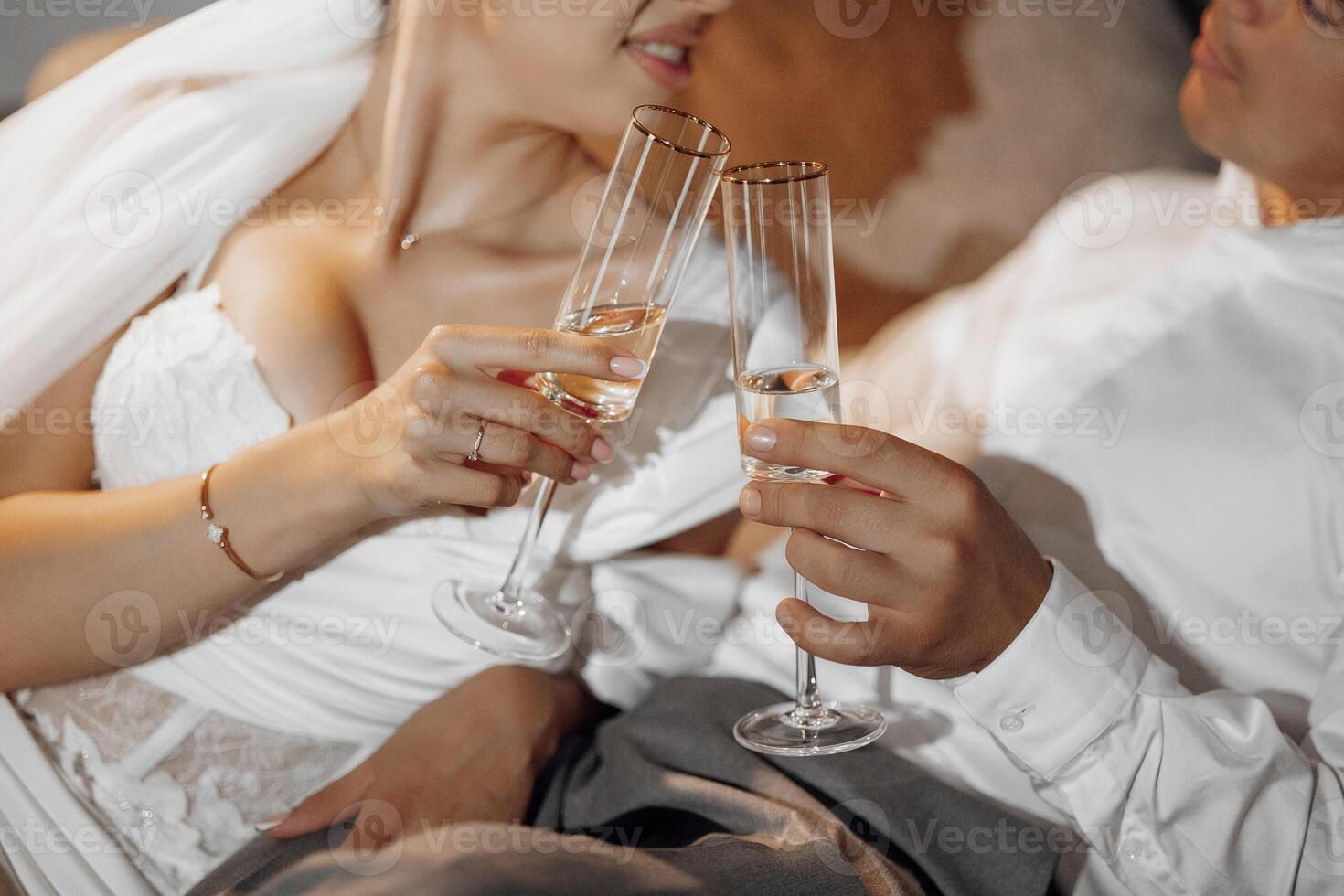 retrato de recién casados en hotel acostado en sofá con lentes de champán, de cerca. el novio suavemente toques el novia. después el Boda ceremonia. contento novia y novio celebrando foto