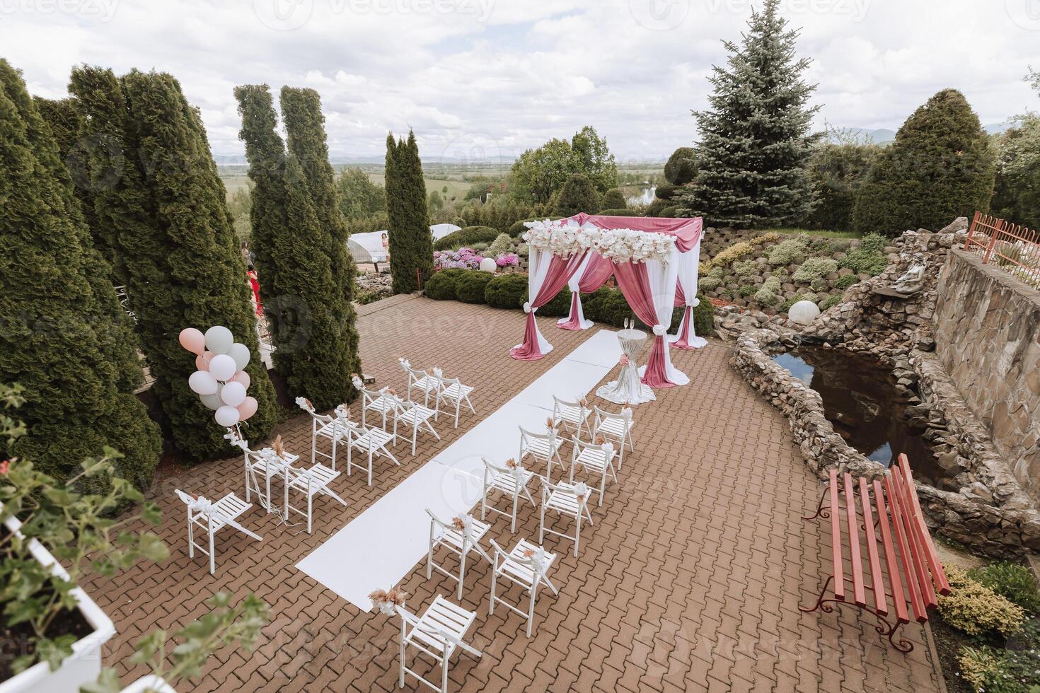 Wedding decor. Many white chairs and a white path. A white and pink arch decorated with flowers. Preparation for the wedding ceremony. Celebration photo