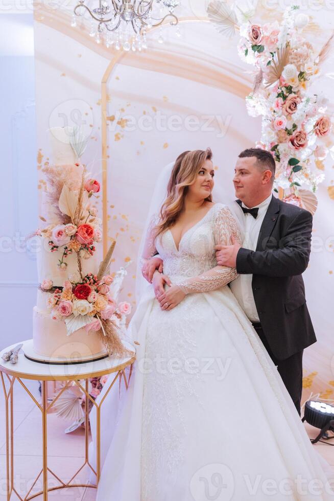 bride and groom near multi-tiered wedding cake decorated with flowers. Beautiful wedding. Incredible brides. photo