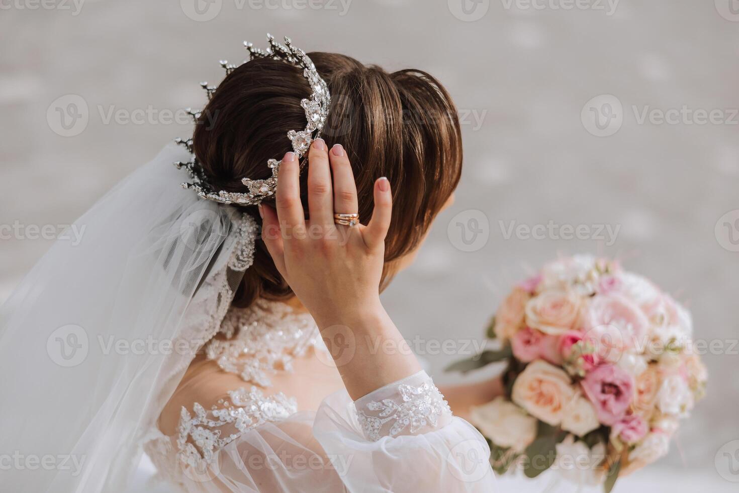 brunette bride in off-the-shoulder lace white dress and tiara posing with a bouquet of white and pink flowers. Beautiful hair and makeup. Spring wedding photo