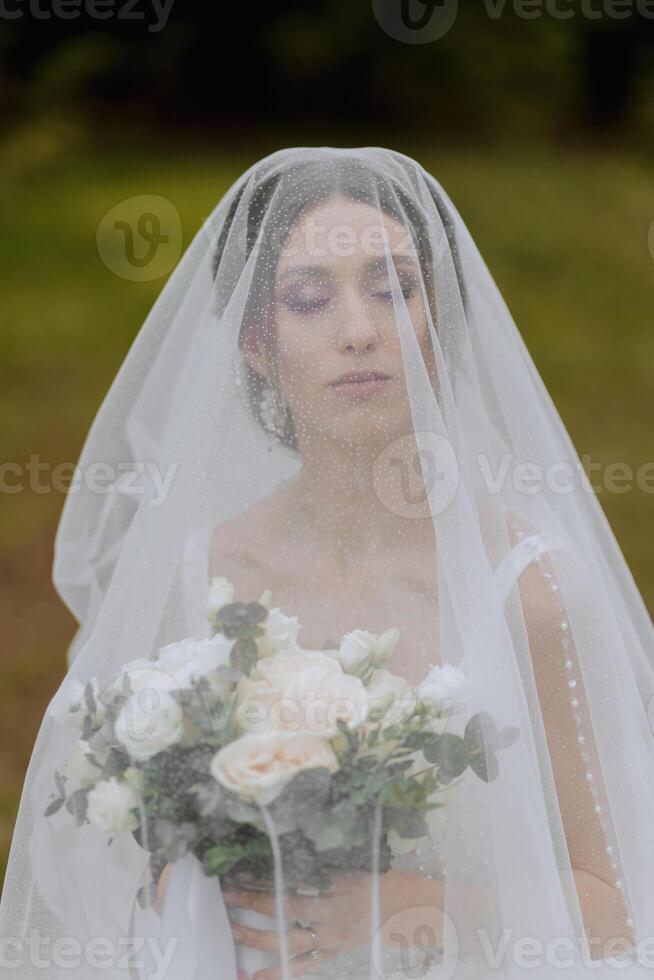 un Pelirrojo novia poses en contra el antecedentes de un floreciente árbol. magnífico vestir con largo mangas, abierto busto. primavera Boda foto