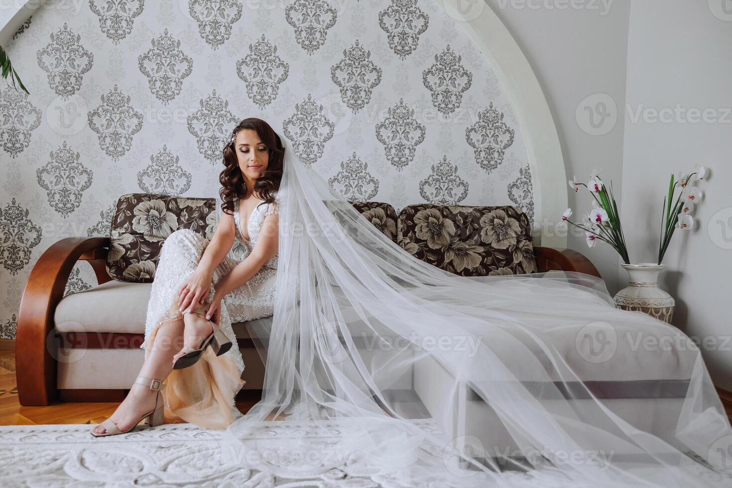 A luxurious bride with a beautiful hairstyle and a gorgeous dress is getting ready for the wedding ceremony in the morning. Morning photo of the bride at home or in a hotel room. Professional makeup.