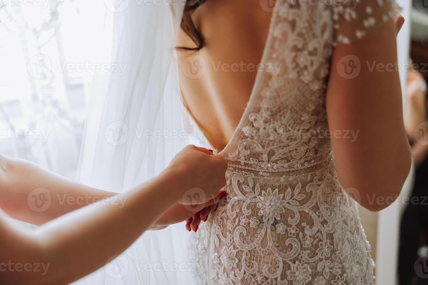Morning of the bride. The bride's maid of honor helps the bride lace up her dress, fasten buttons on the dress or sleeves. Girlfriends help the bride fasten her dress photo