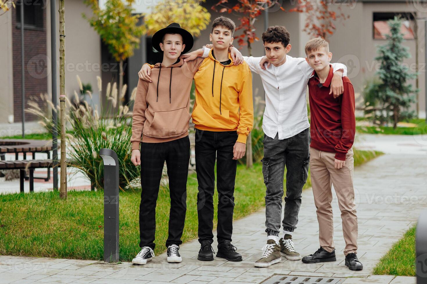 Group of smiling and happy teenage friends wearing casual clothes spending time together, posing and talking with each other near college building on autumn day. photo