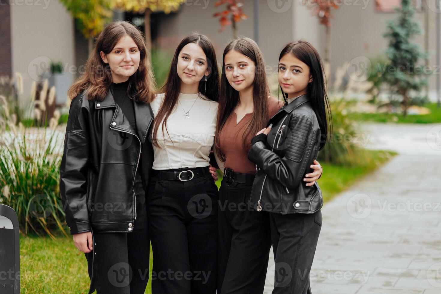 Group of smiling and happy teenage friends wearing casual clothes spending time together, posing and talking with each other near college building on autumn day. photo