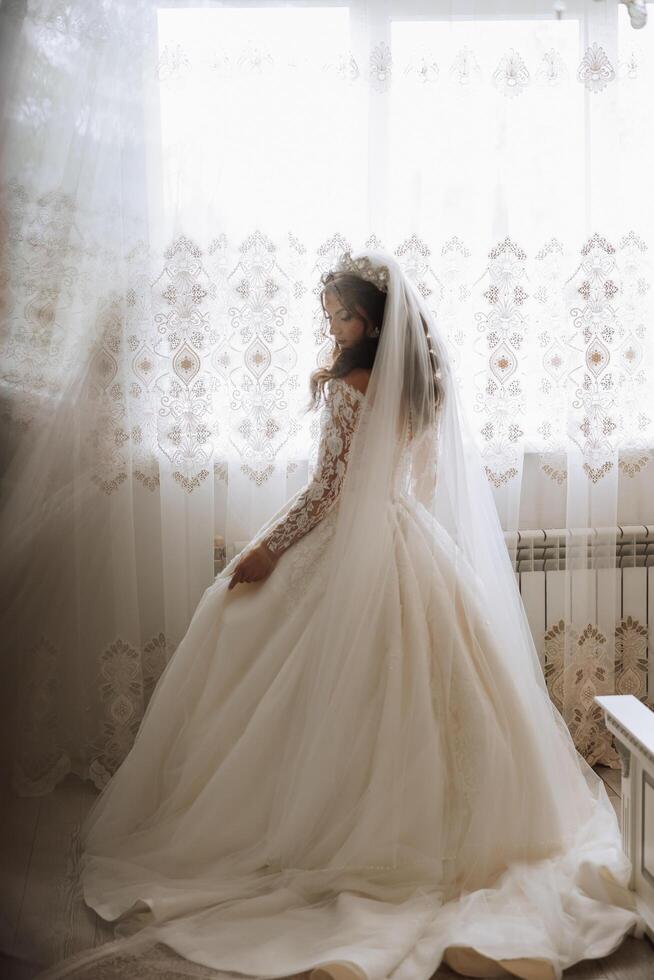 un lujoso novia con un hermosa peinado y un maravilloso vestir es consiguiendo Listo para el Boda ceremonia en el Mañana. Mañana foto de el novia a hogar o en un hotel habitación. profesional constituir.