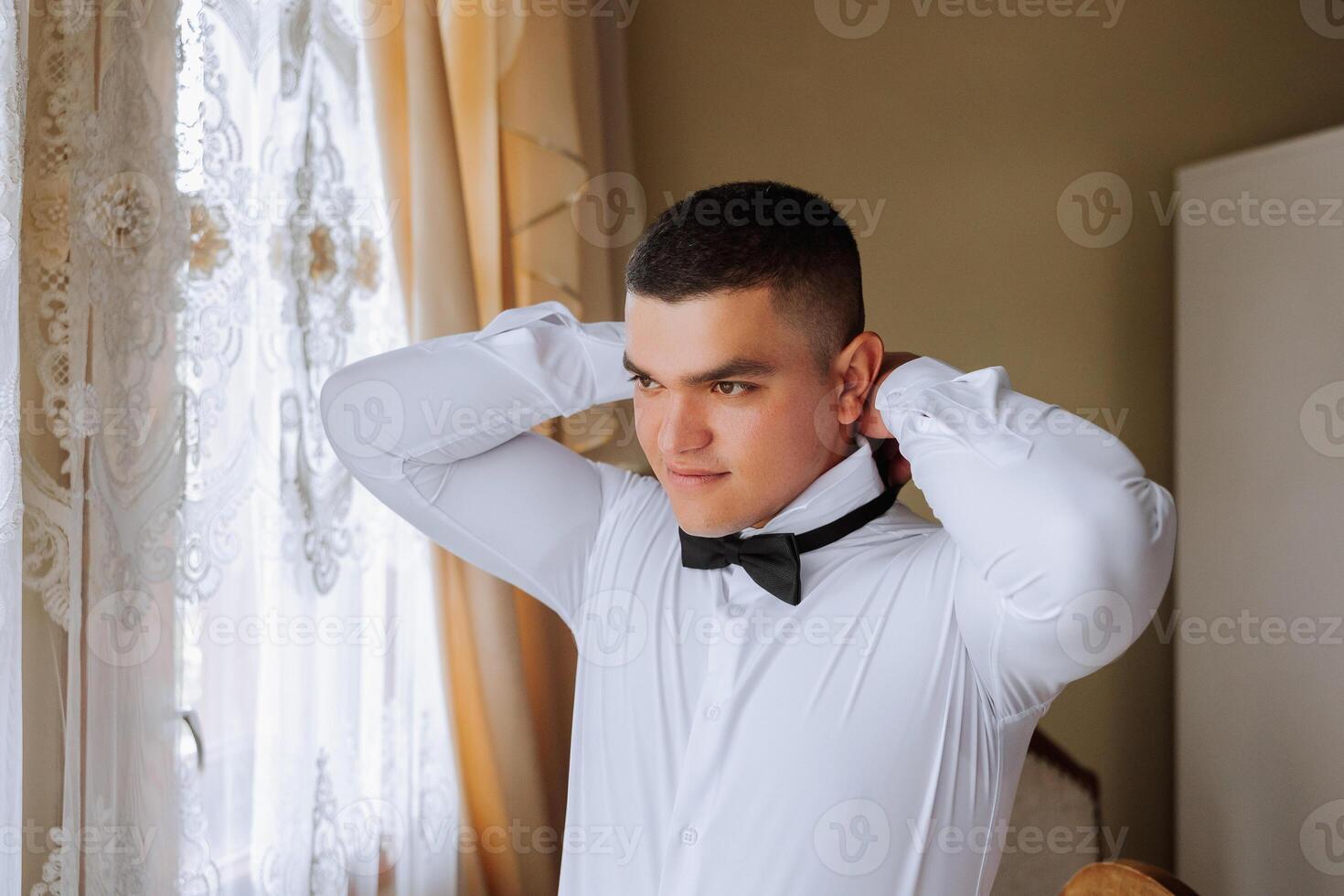 A stylish groom is tying his tie, preparing for the wedding ceremony. Groom's morning. A businessman wears a tie. The groom is getting ready in the morning before the wedding ceremony. photo