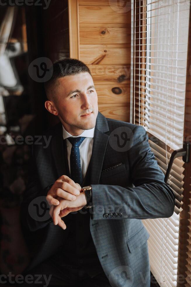A stylish portrait of the groom preparing for the wedding ceremony in the morning. Groom's morning. Preparation for the groom's morning. The groom puts on a jacket. The confident look of a mature man. photo