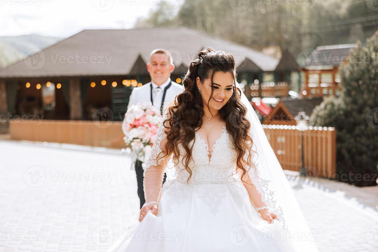 A beautiful young bride, in a summer park, walks ahead of her groom. Beautiful wedding white dress. Walks in the park. A happy and loving couple. photo