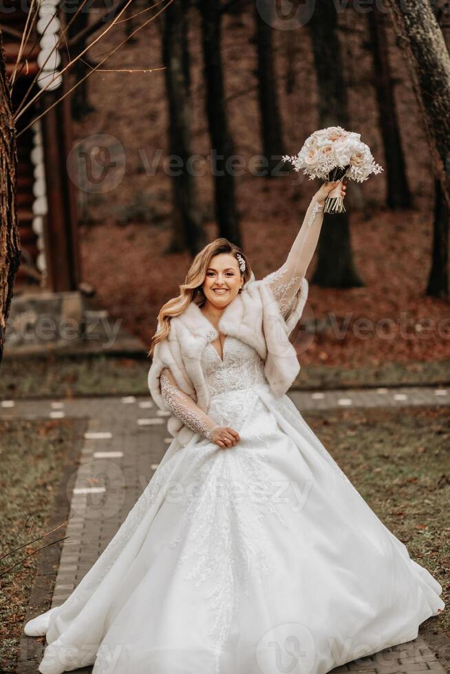 Beautiful bride with a wedding bouquet of flowers, attractive woman in a wedding dress with a long veil. Happy bride woman. Bride with wedding makeup and hairdo. Winter wedding photo