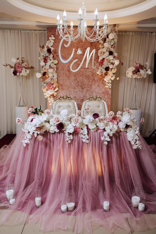 Romantic table setting in a restaurant for a holiday. Wedding decor for the newlyweds at the banquet. Floristry of fresh flowers and candles, boho style. Catering for the bride and guests. photo