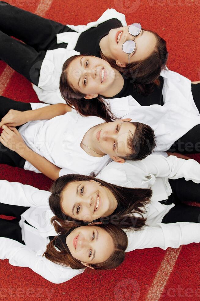 Happy friends lying together in a circle looking at the camera, holding hands and smiling while lying on a red wall... Friendship, lifestyle, togetherness, business and teamwork concepts. photo