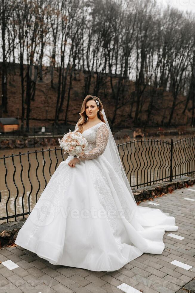 Beautiful bride with a wedding bouquet of flowers, attractive woman in a wedding dress with a long veil. Happy bride woman. Bride with wedding makeup and hairdo. Winter wedding photo
