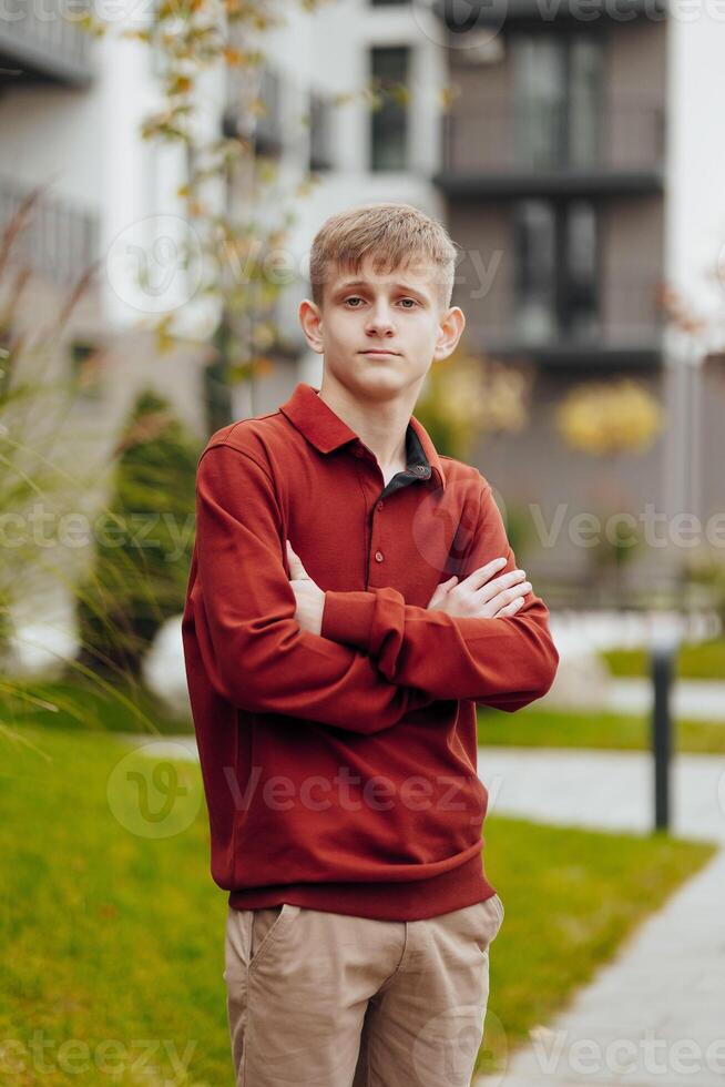 Vertical close-up portrait of a teenager in casual clothes. Happy smiling teenager in autumn park in sunlight. A beautiful child looks at the camera in nature. photo