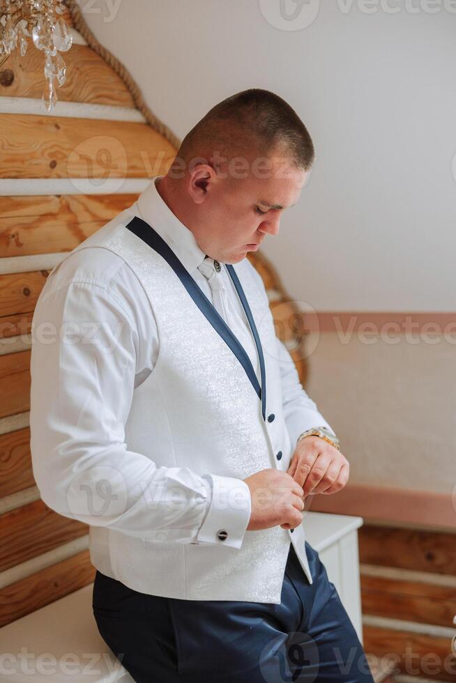 The groom fastens a button on his vest at the groom's morning gatherings. Groom wedding preparation. photo