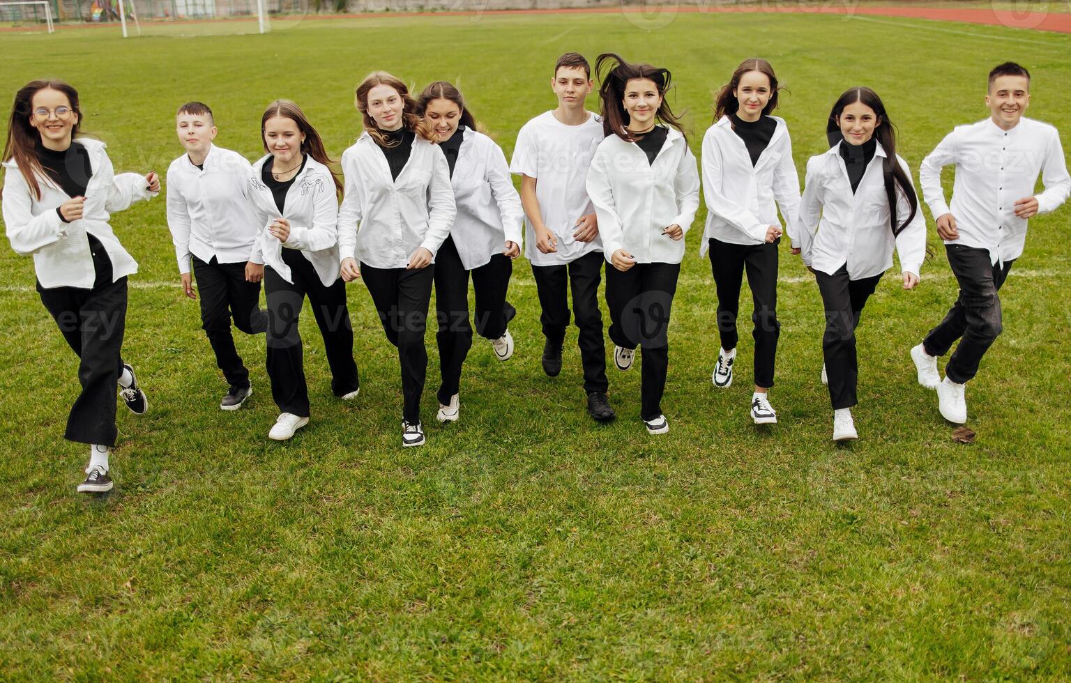 A group of many happy teenagers dressed in the same outfit having fun and posing in a stadium near a college. Concept of friendship, moments of happiness. School friendship photo