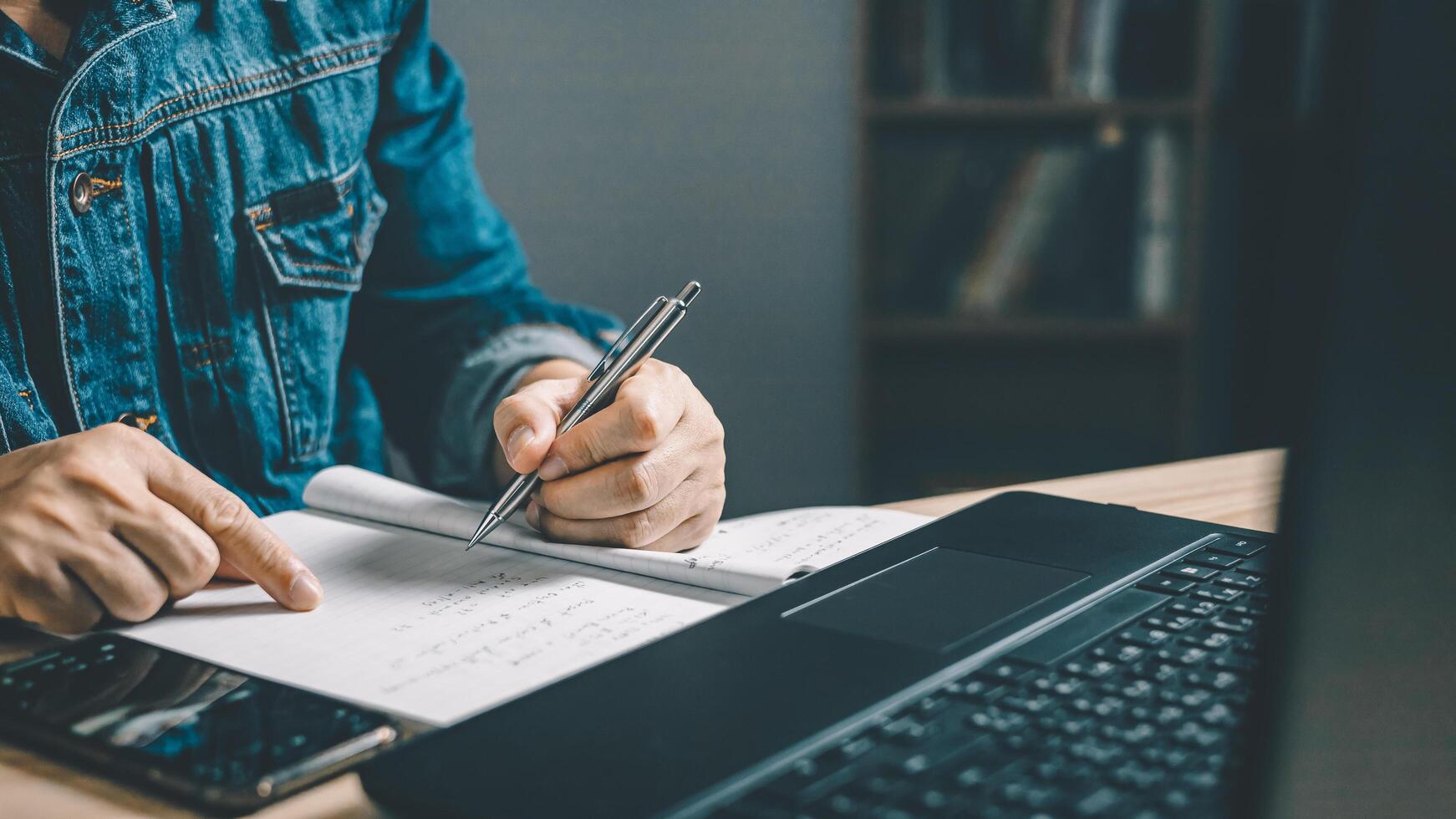 Man using smartphone and taking notes in planning. which is payment online, sits on the chair in the living room at home on a desktop. The concept of finance and online shopping. photo