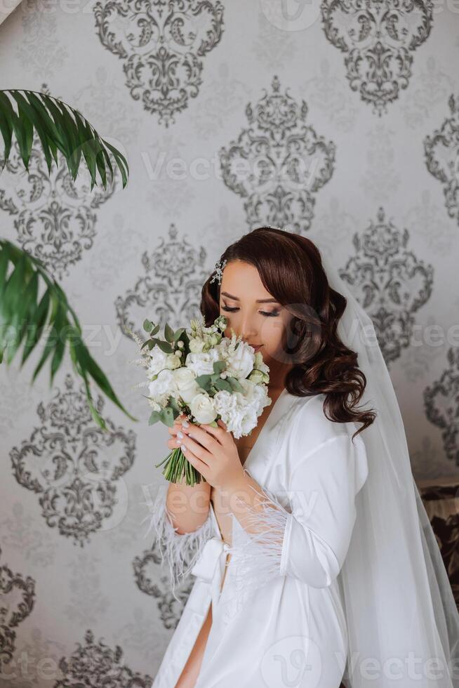 A beautiful brunette bride with a tiara in her hair is getting ready for the wedding in a beautiful robe in boudoir style. Close-up wedding portrait, photo. photo