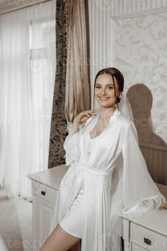 retrato de novia niña en blanco túnica con profesional peinado y natural maquillaje en hotel habitación con maravilloso interior foto