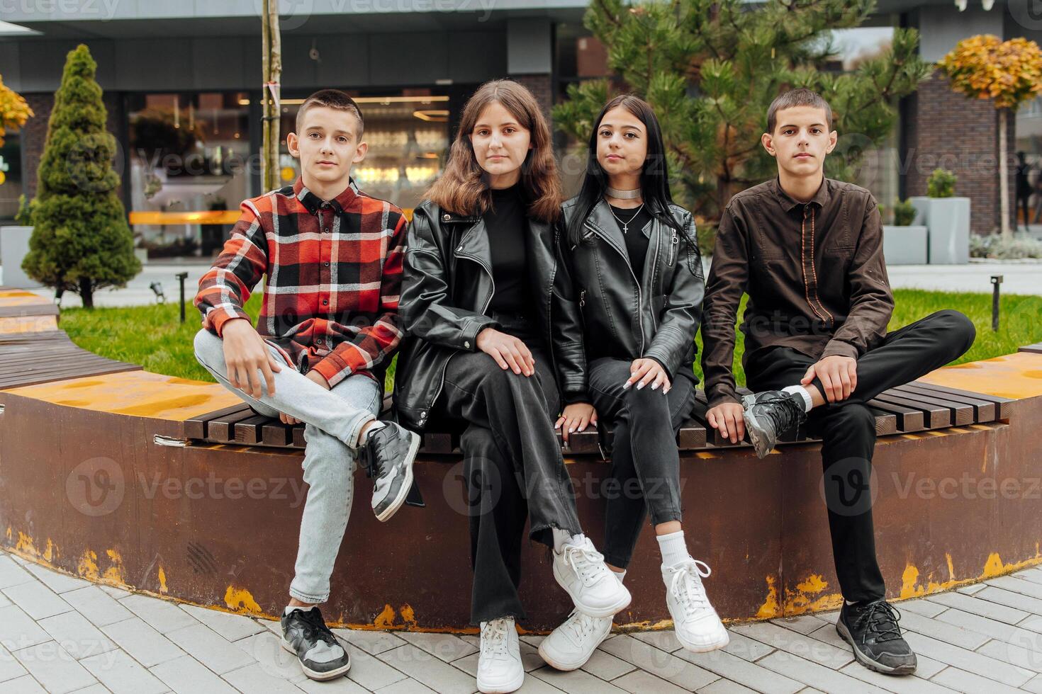 Group of smiling and happy teenage friends wearing casual clothes spending time together, posing and talking with each other near college building on autumn day. photo