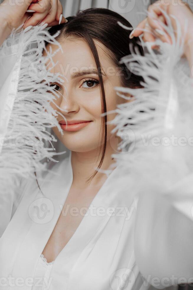 portrait of bride girl in white gown with professional hairstyle and natural makeup in hotel room with reflection in window. The best day photo