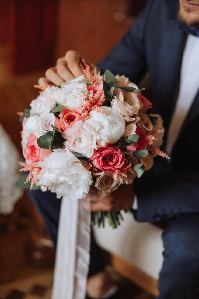 Stylish portrait of the groom with a bouquet of flowers. A man is preparing for a wedding ceremony in the morning. Groom's morning. Preparation for the groom's morning. Young and handsome groom. photo