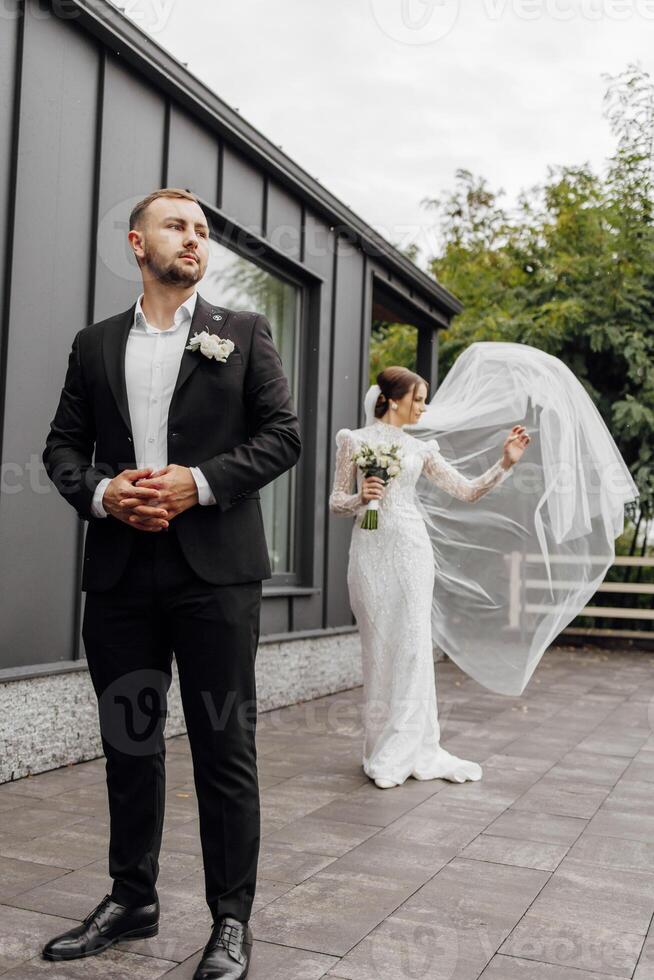 The bride in a fashionable dress and a veil. Groom in a black suit in the foreground. The concept of a beautiful wedding. photo