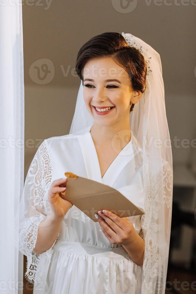 el novia en un seda traje con un velo poses en su habitación. Mañana de el novia. preparación. Boda fotografía foto