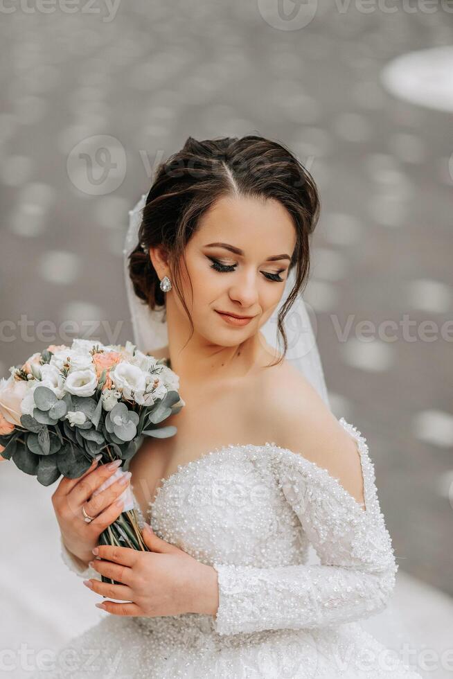 The bride in a white dress with a train and a long veil poses in nature, holding a bouquet. Walk. Winter wedding in nature. photo
