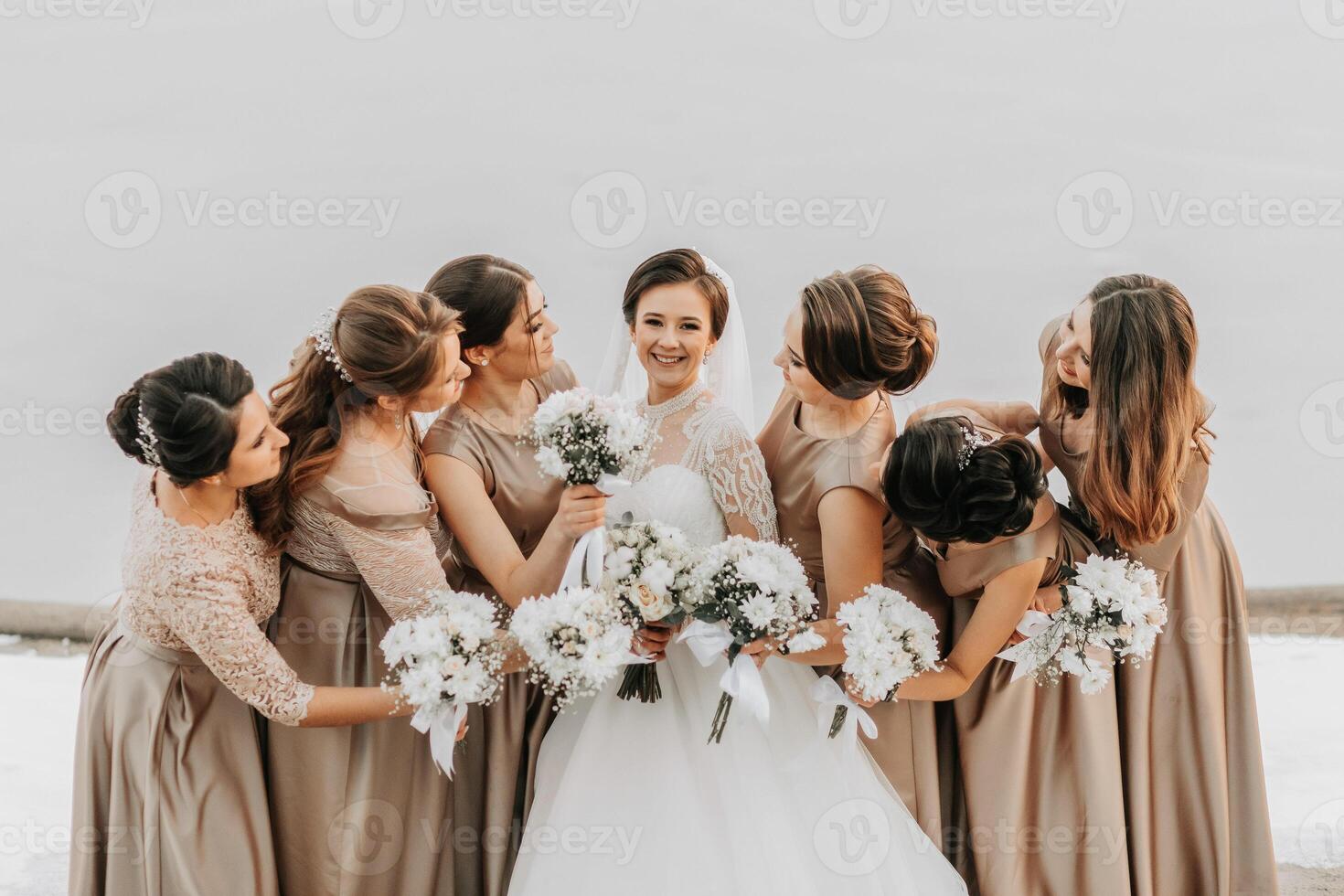 The bride and her bridesmaids pose holding bouquets and looking at the bride photo