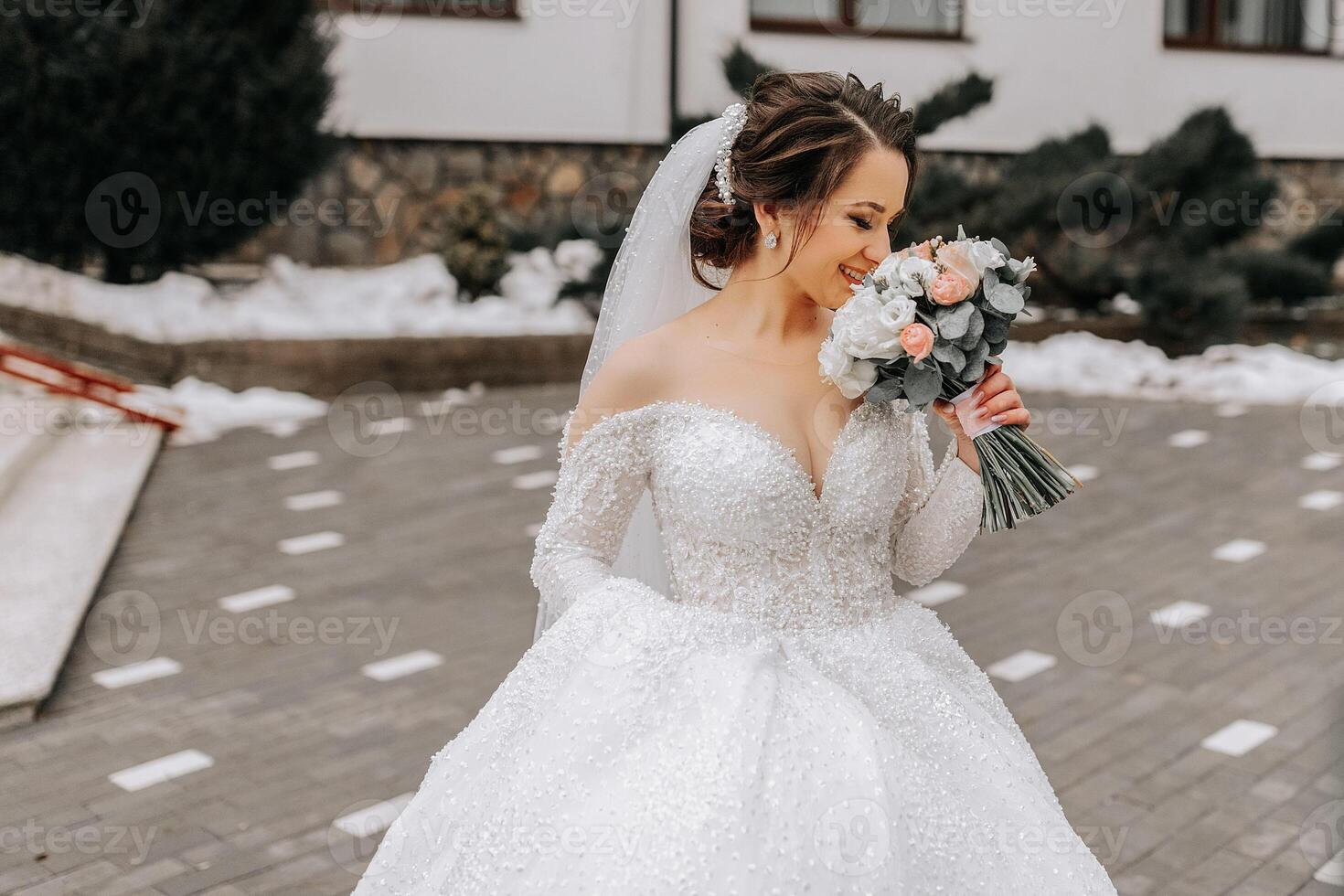 The bride in a white dress with a train and a long veil poses in nature, holding a bouquet. Walk. Winter wedding in nature. photo