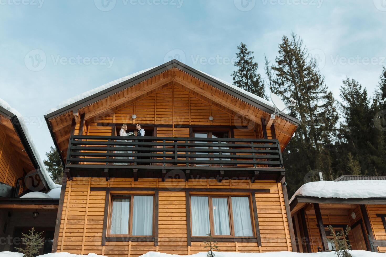 winter wedding in a wooden cottage in the mountains. The bride and groom celebrate their wedding in winter. The groom hugs the bride on the balcony. photo