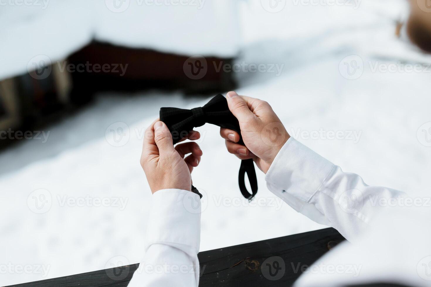 Close-up portrait of a young man tying a bow tie on his collar while fixing a black bow on a white shirt photo