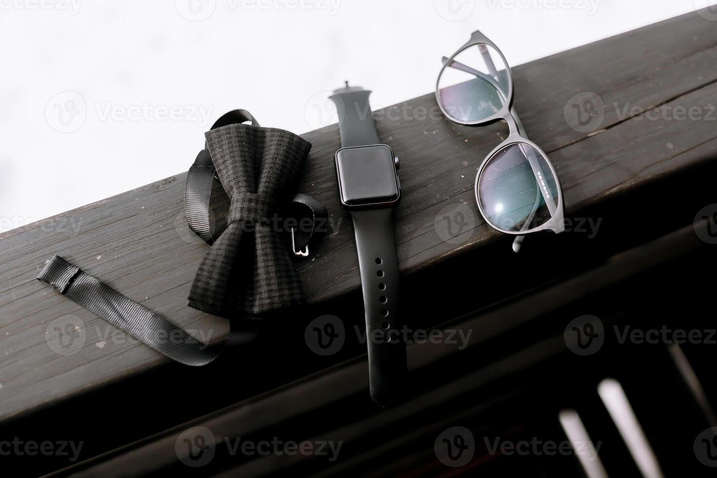 Outfit of traveler, student, teenager, hipster. Top view of essentials for modern young person. Sunglasses, bow tie, watch on black wooden background photo