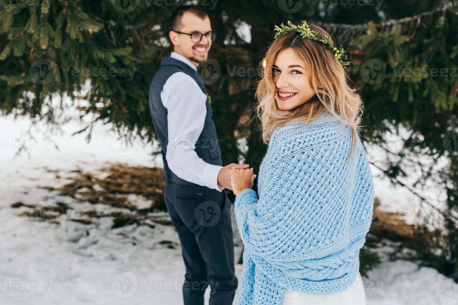 Happy and smiling bride and groom on the background of winter forest. A handsome groom gently holds his bride's hand and leads her away. The concept of a modern winter wedding. photo
